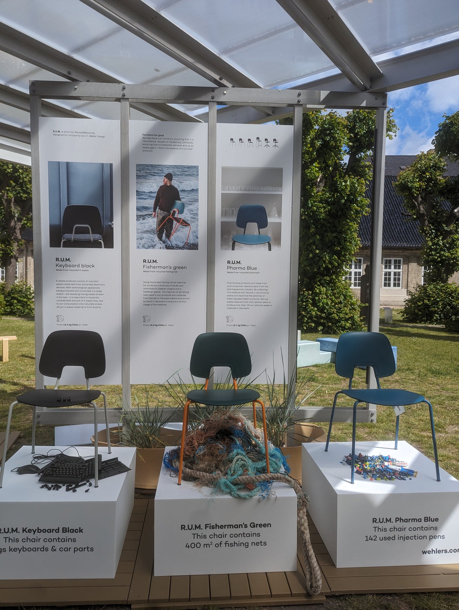 The Wehlers R.U.M. chair collection on display at a design exhibition, showcasing the 100% recycled material options: Fisherman's Green, Keyboard Black, and Pharma Blue.